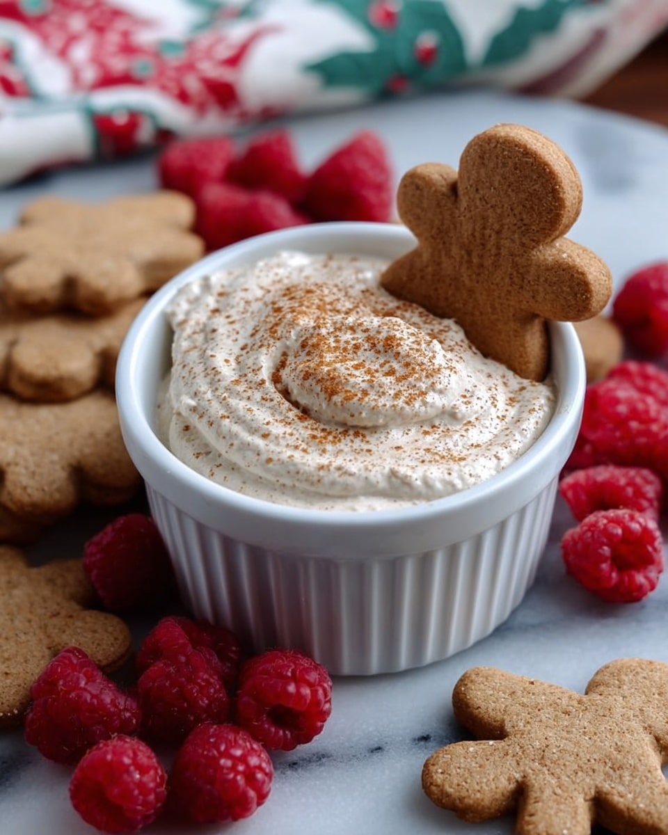 A white ramekin filled with a thick, creamy light beige dip topped with a light dusting of brown spice, with a small gingerbread cookie shaped like a flower placed standing on the edge of the ramekin, surrounded by more gingerbread cookies and fresh red raspberries on a white marbled surface with a red and white cloth partially visible in the background photo taken with an iphone --ar 4:5 --v 7