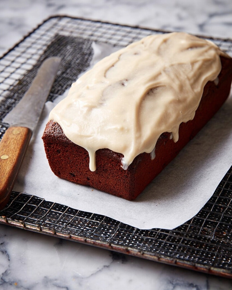 A rectangular, dark brown cake with a smooth, creamy light beige frosting spread thickly over the top, slightly dripping down the sides. The cake sits on a wire cooling rack lined with white parchment paper, which is placed on a black tray with a textured pattern. A knife with a wooden handle rests beside the cake, all set on a white marbled surface. Photo taken with an iphone --ar 4:5 --v 7