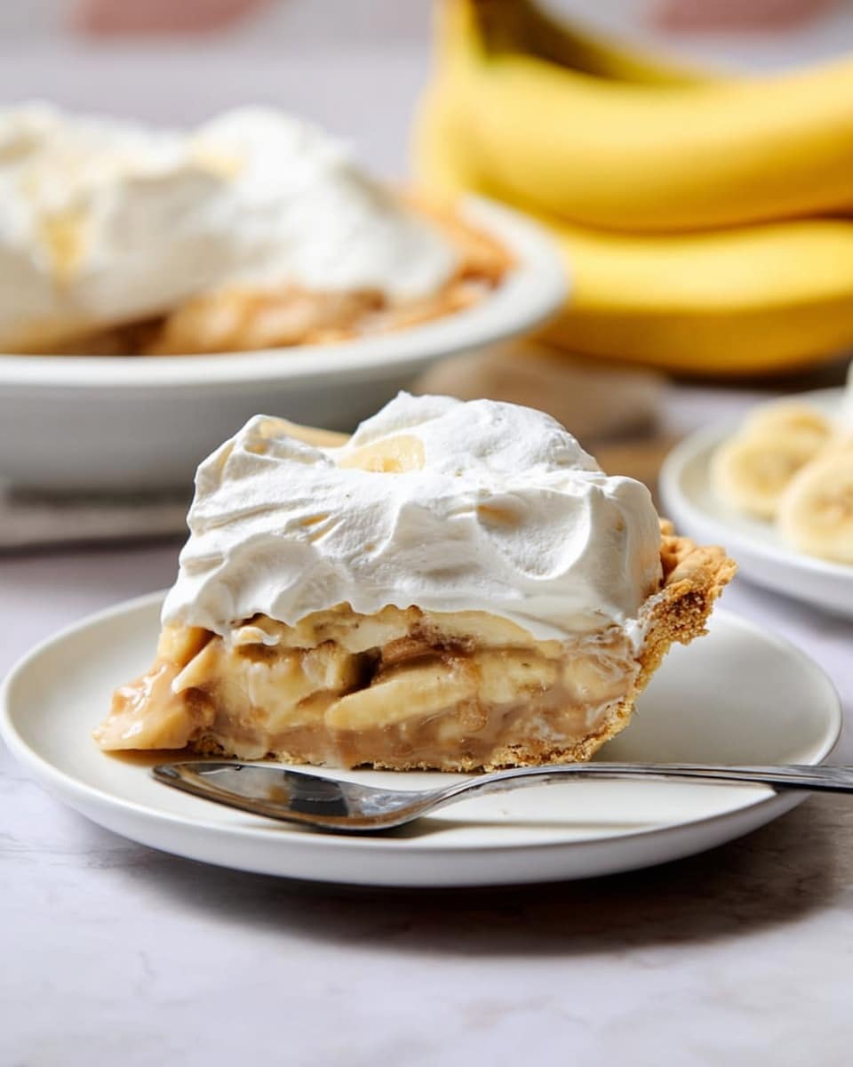 A slice of pie is placed on a white plate, showing three clear layers: the bottom is a golden, flaky crust, the middle is a creamy light brown filling with pieces of banana inside, and the top is a thick, fluffy layer of white whipped cream. A silver spoon rests on the plate next to the slice. Behind the plate, there is another white plate with whole yellow bananas resting on a white marbled surface. The photo looks bright and soft, focused on the pie slice. Photo taken with an iphone --ar 4:5 --v 7