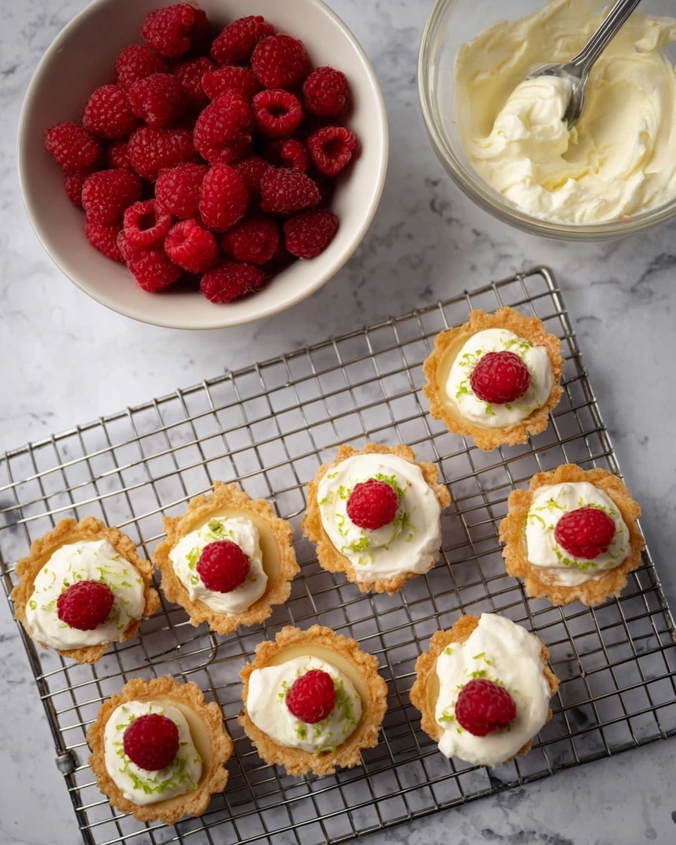 The image shows small tart shells with a light golden brown, crispy texture arranged on a metal cooling rack over a white marbled surface. Each tart shell has three layers: the base is the shell, the middle layer is creamy white filling with a smooth texture, and the top layer is decorated either with small green lime zest or a single bright red raspberry placed at the center. The raspberries have a bumpy surface and vibrant color, giving a fresh look. To the left, there is a white bowl filled with more red raspberries, and to the right, a clear glass bowl holds extra creamy white filling with a spoon inside. photo taken with an iphone --ar 4:5 --v 7