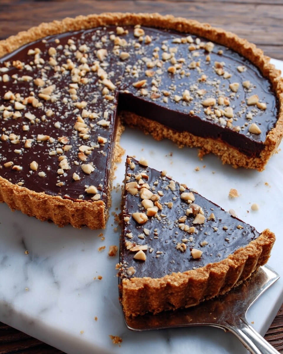 A round tart with a golden-brown crumbly crust looks crisp and thick, holding a dark, glossy chocolate layer spread evenly on top. The chocolate layer is smooth with small bits giving it a slightly bumpy texture, scattered with chopped light brown nuts. One slice is lifted on a silver spatula, showing the tart’s depth and the textured crust edge holding the chocolate layer tightly. The tart sits on a white marbled surface with a few crumbs around it. Photo taken with an iphone --ar 4:5 --v 7