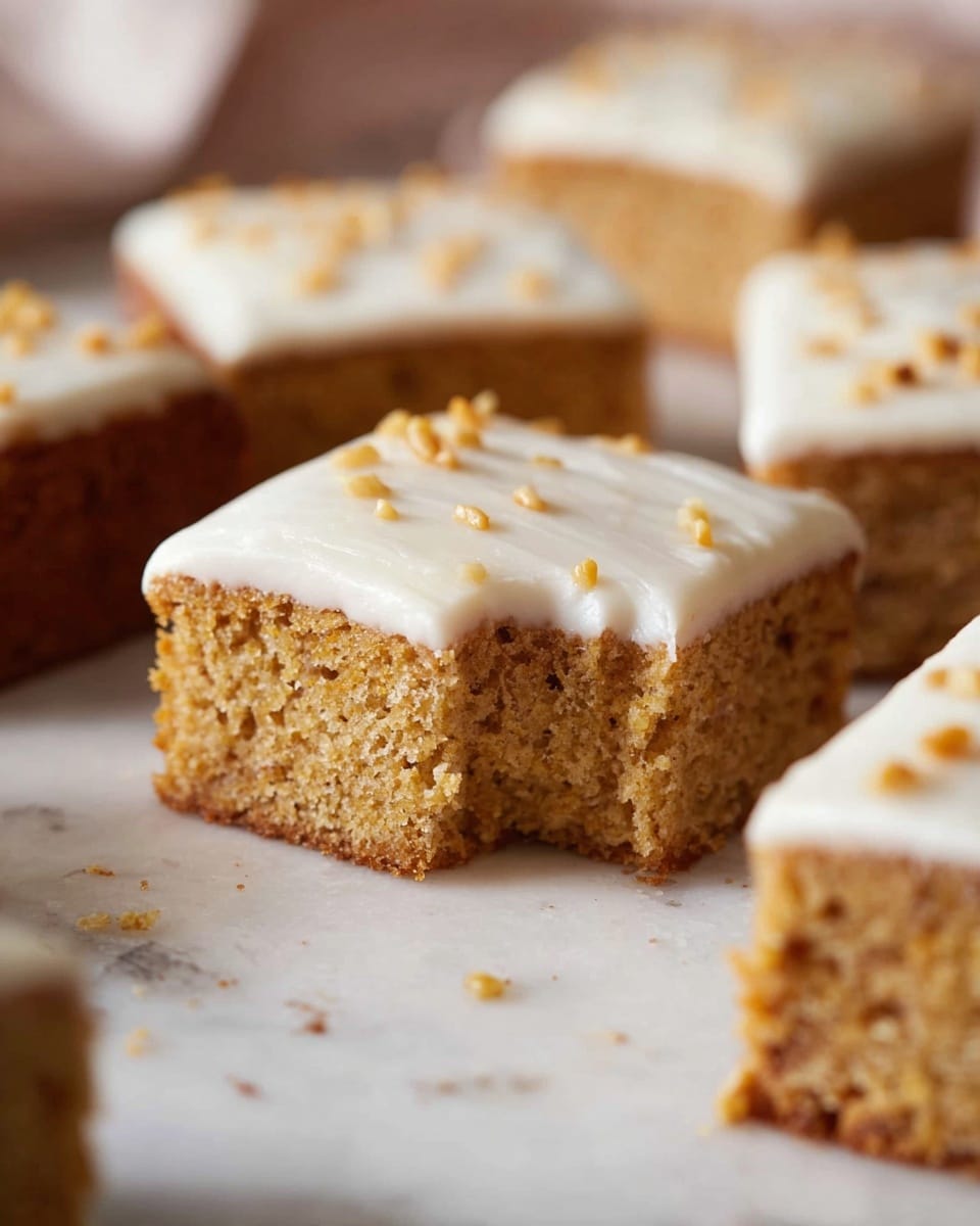 The image shows several square pieces of cake arranged on a white marbled surface. Each piece has two layers: a thick, soft, light brown cake base with a textured crumb, and a smooth, white icing layer on top sprinkled with small light brown bits. One piece in the front has a small bite taken out of it, displaying the inner softness and moist texture of the cake. The background is softly blurred, emphasizing the cake pieces in the foreground. photo taken with an iphone --ar 4:5 --v 7