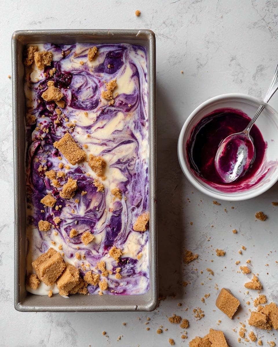 A rectangular dessert tray filled with a creamy white and deep purple swirled mixture, topped with scattered light brown crushed pieces that add texture. To the right, there is a white bowl with a shiny silver spoon inside, coated in vibrant purple sauce, alongside some broken light brown crumbs scattered around it. The background is a white marbled texture. photo taken with an iphone --ar 4:5 --v 7