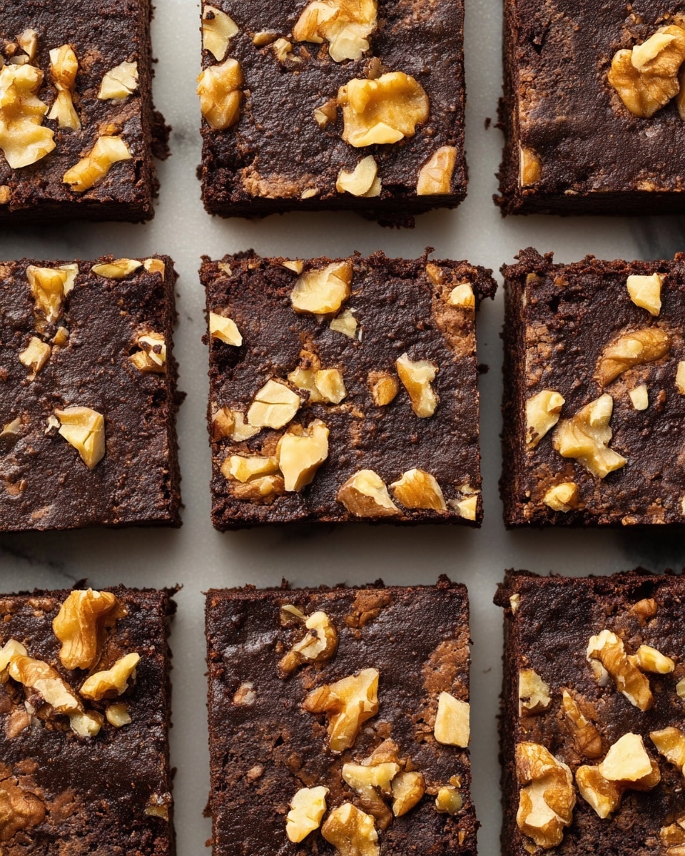 The image shows a close-up of a grid of nine dark brown chocolate brownies with a slightly crumbly texture. Each brownie is square and topped with uneven pieces of light tan and golden walnut halves and chunks spread across the surface. The brownies are placed closely together on a white marbled textured surface, with clear straight lines of space visible between each piece. The overall look is rich and rustic with contrast between the deep chocolate and the golden nuts. photo taken with an iphone --ar 4:5 --v 7
