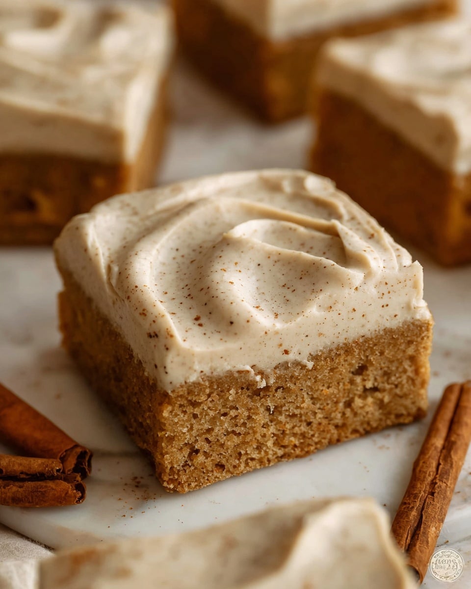 The image shows a single square piece of cake with two visible layers; the bottom layer is a moist, light brown cake, while the top layer is a thick, creamy frosting with a light beige color and tiny brown specks spread evenly across it in swirled patterns. The cake sits on a white marbled surface with whole cinnamon sticks placed nearby, adding a warm touch. Other similar pieces of cake are slightly out of focus in the background, giving a cozy and inviting feeling. photo taken with an iphone --ar 4:5 --v 7