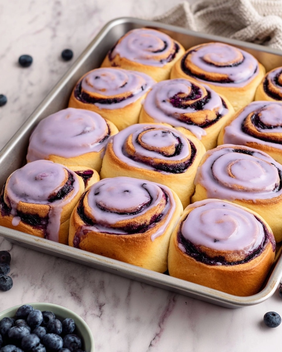 The image shows a metal tray filled with twelve soft, swirled rolls arranged in four rows of three. Each roll consists of a golden-brown dough base with a dark purple filling that spirals from the center outward. About half of the rolls are topped with a smooth, glossy lavender icing that drips slightly over the edges, adding a creamy texture and more purple color. The tray is placed on a white marbled surface, with scattered fresh blueberries and a small bowl filled with more blueberries around it. photo taken with an iphone --ar 4:5 --v 7