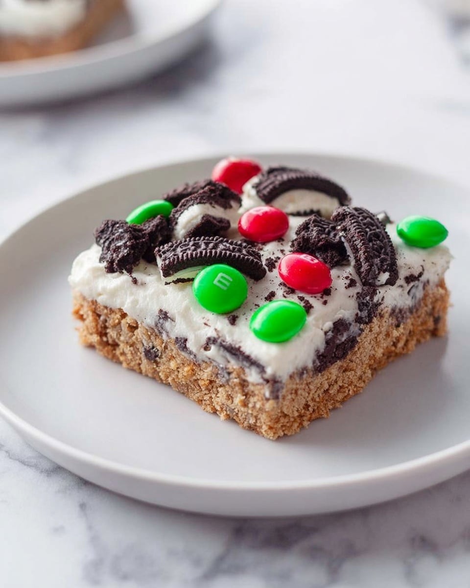 A single square bar is shown on a white plate, resting on a white marbled surface. The bar has two main layers: the bottom layer is a light brown base with a textured, crumbly look, while the top layer is a thick, smooth white frosting. On top of the frosting, there are broken pieces of dark chocolate sandwich cookies arranged unevenly, with some pieces showing white cream inside. Scattered among the cookies are bright red and green candy-coated chocolates, adding a festive touch. The overall look is colorful and inviting, with a mix of rough and smooth textures. Photo taken with an iphone --ar 4:5 --v 7
