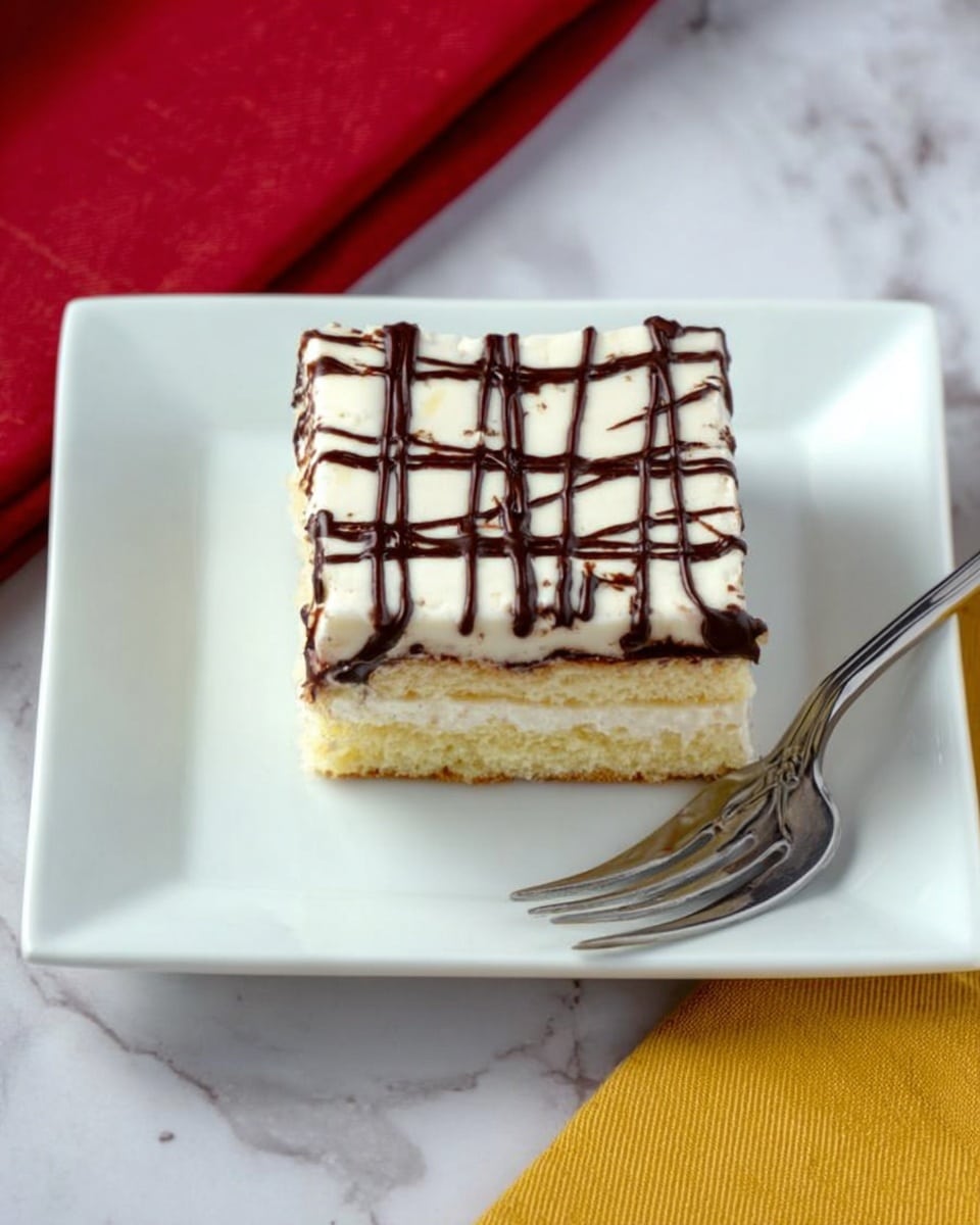 A white square piece of cake sits on a white square plate with a silver fork resting on the right side of the plate. The cake has three visible layers: a light yellow cake layer at the bottom, a thin layer of cream in the middle, and a thick white icing layer on top. Dark chocolate lines are drizzled over the top icing in a crisscross pattern. The plate is placed on a white marbled surface with a red napkin on the left and a yellow cloth in the upper background. Photo taken with an iphone --ar 4:5 --v 7