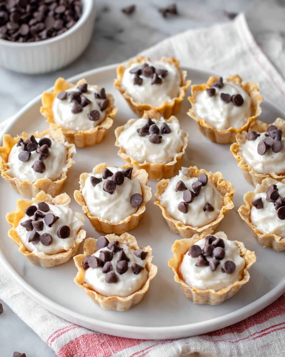 The image shows a round white plate on a white marbled surface with twelve small tart cups arranged in a neat pattern. Each tart cup has a light golden-brown, crinkled shell filled with a smooth, white creamy filling. On top of the cream in each cup, there are several small dark chocolate chips scattered, adding a contrast of color and texture. The background includes a white bowl filled with more chocolate chips and a white cloth with red stripes near the edge of the plate. The photo taken with an iphone --ar 4:5 --v 7