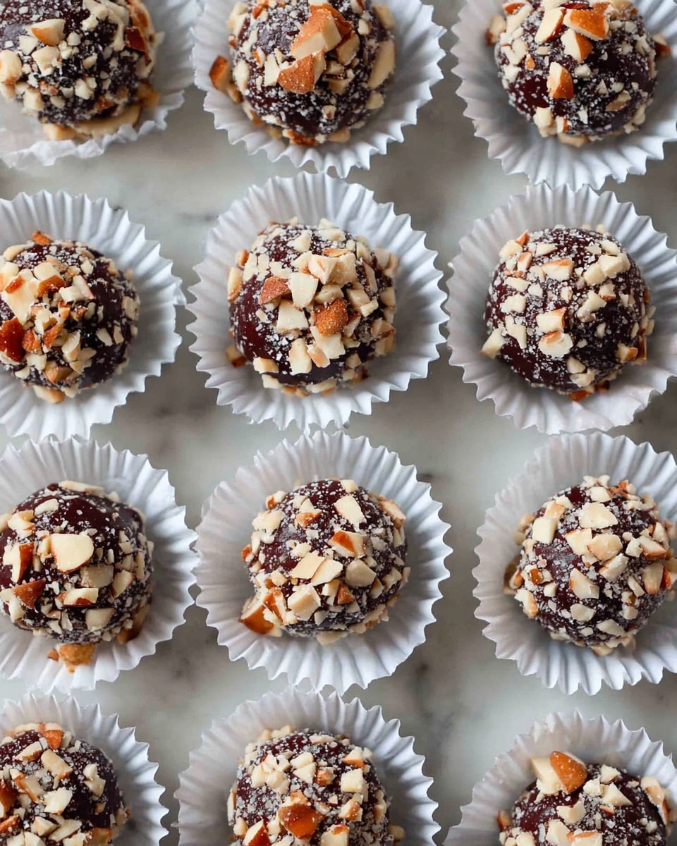 The image shows many round chocolate balls covered with chopped nuts on the outside. Each ball is placed neatly in a white pleated paper cup, with the chocolate showing through the nut pieces, creating a rich dark brown and off-white textured look. The balls are laid out in a grid pattern on a white marbled surface, giving a clean and elegant background. photo taken with an iphone --ar 4:5 --v 7