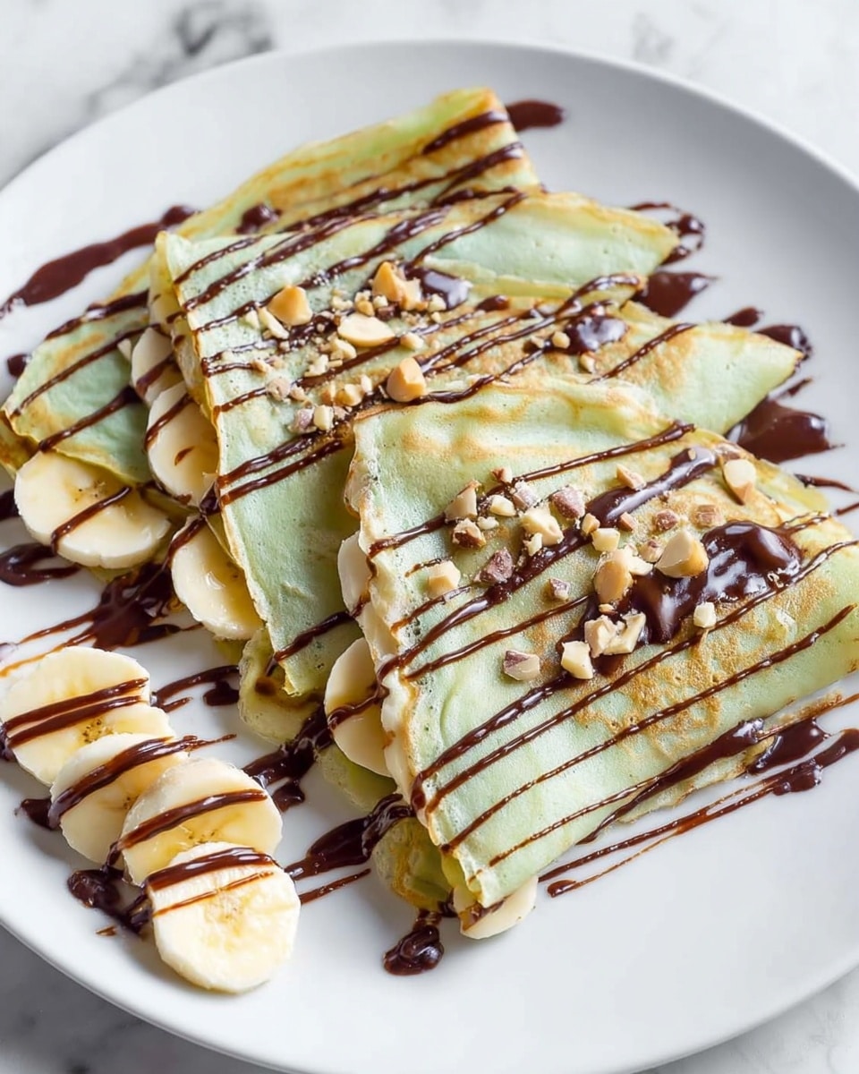 The image shows three folded thin crepes with a pale green tint, each folded twice to create triangular shapes on a white plate. Inside the crepes, creamy white layers are visible, likely banana slices and cream. The crepes are topped and drizzled with dark chocolate sauce in thin lines, which also spreads across the plate. Small pieces of light brown nuts are scattered on top and around the crepes. To the side of the plate, a small pile of banana slices also has dark chocolate sauce drizzled over it. The plate rests on a white marbled surface. Photo taken with an iphone --ar 4:5 --v 7
