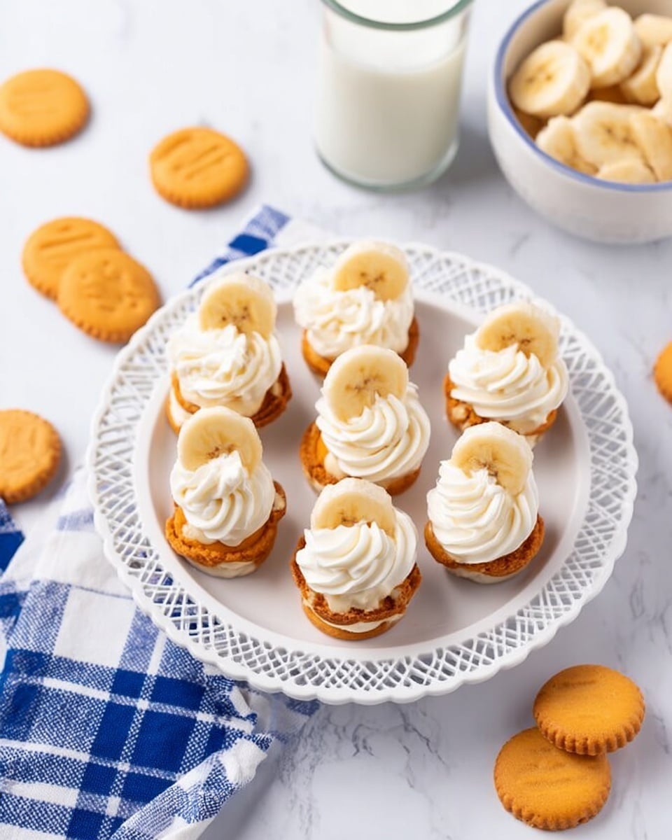 A white plate with a decorative open-weave rim holds eight small round layered treats. Each treat has two light orange cookie-like layers on the bottom and top. Between the layers is a swirl of white cream, and on top of each treat are a few slices of banana arranged neatly with additional dollops of white cream. The plate sits on a white marbled surface scattered with round orange cookies. A small white bowl filled with banana slices and a glass of milk are nearby. A blue and white checkered cloth is partly visible on the side. Photo taken with an iphone --ar 4:5 --v 7