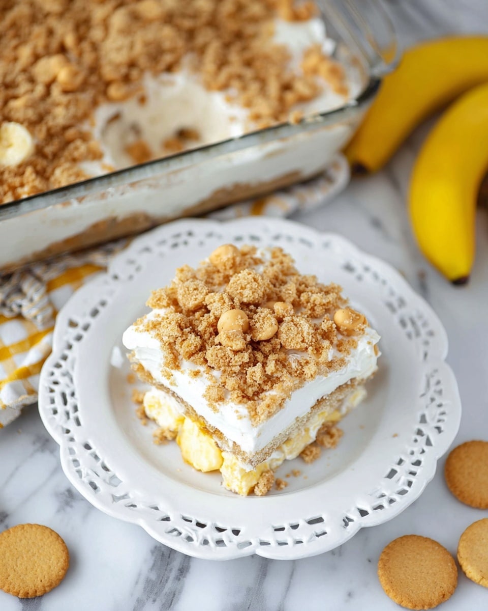 A square piece of layered dessert sits on a white plate with a lacy edge, placed on a white marbled surface. The dessert has three visible layers: a bottom layer of yellow cake, a middle layer of white creamy filling, and a top layer covered with crushed light brown cookies and banana chips, giving a crumbly texture. In the background, a glass baking dish holds more of the same dessert, with the top layer thickly covered in cookie crumbs. Some whole light brown cookies and a yellow banana are scattered around on the white marbled surface. Photo taken with an iphone --ar 4:5 --v 7
