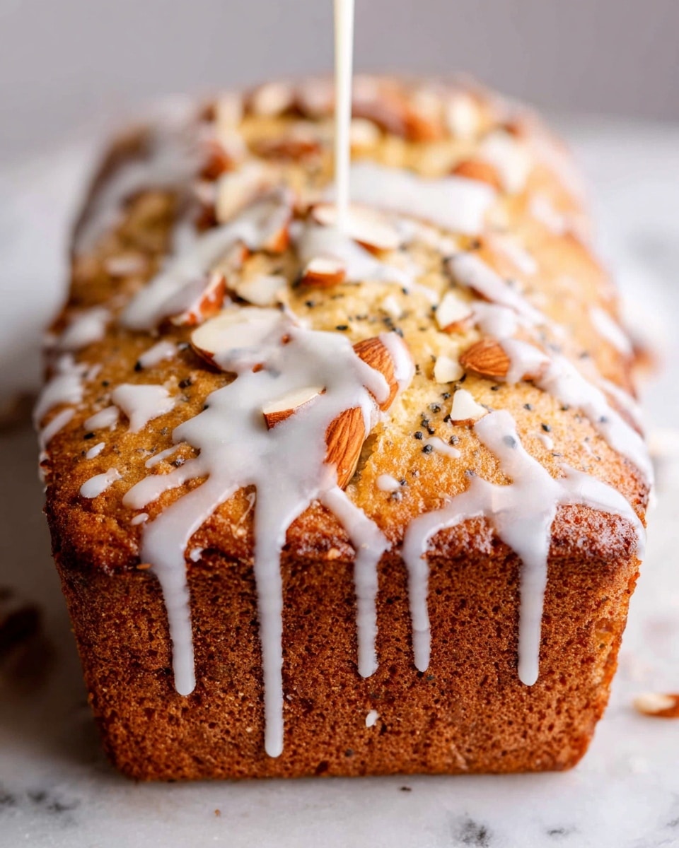 A golden brown loaf cake with a slightly rough texture sits on a white marbled surface. The top of the loaf has visible pieces of chopped almonds scattered across it and poppy seeds embedded in the cake. White glaze is being drizzled over the top from above, creating thick, uneven lines running down the sides. The bottom edge of the loaf is darker and slightly ridged from the baking pan. photo taken with an iphone --ar 4:5 --v 7
