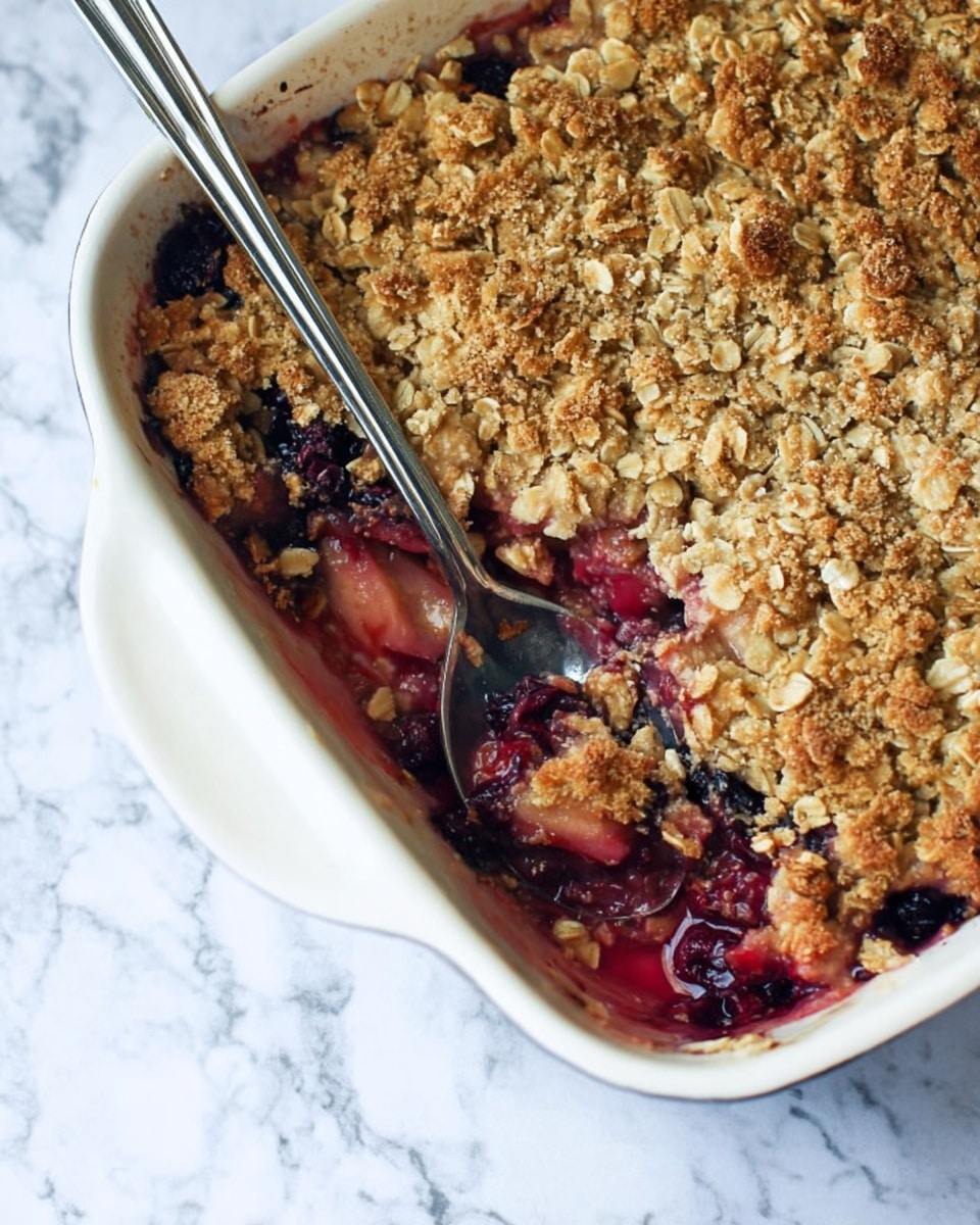 A creamy white baking dish filled with a fruit crumble that has two main layers: the top layer is golden brown with baked oats and a crumbly texture, showing some browned sugar sprinkled unevenly across, while underneath the fruit layer is deep red and purple, likely berries, with visible juice bubbling around the edges where a silver spoon scoops into it from the right side. The dish sits on a white marbled surface, and the spoon handle rests inside the dish. photo taken with an iphone --ar 4:5 --v 7