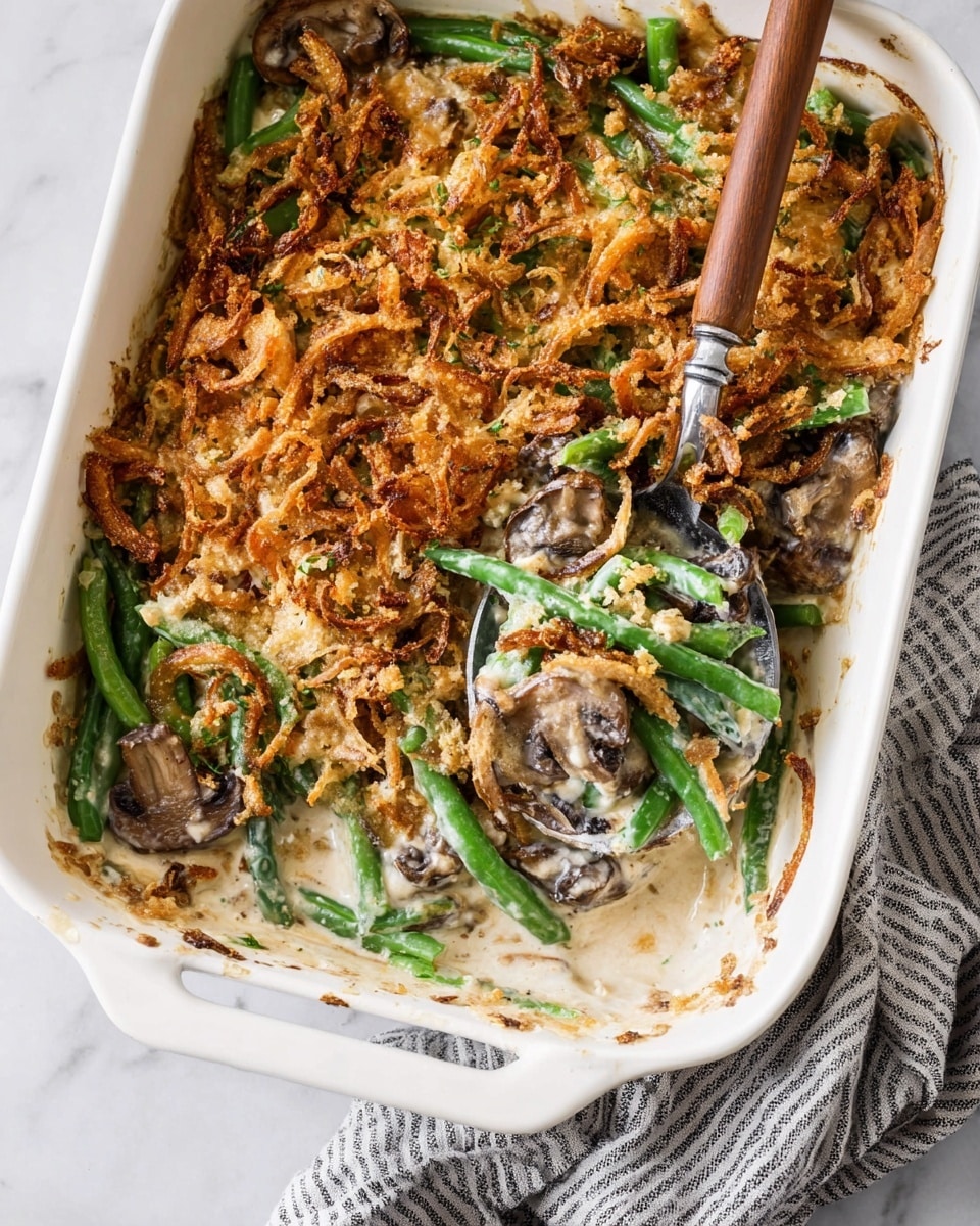 A white square casserole dish holds a green bean casserole with three visible layers. The bottom layer is a creamy sauce mixed with sliced brown mushrooms. The middle layer has bright green, fresh green beans immersed in the sauce. The top layer is a golden-brown crispy fried onion topping, spread unevenly over the beans and sauce, adding texture. A spoon with a wooden handle is inside the dish, lifting some green beans mixed with creamy sauce and mushrooms. The dish rests on a white marbled surface with a gray and white striped cloth beside it. photo taken with an iphone --ar 4:5 --v 7