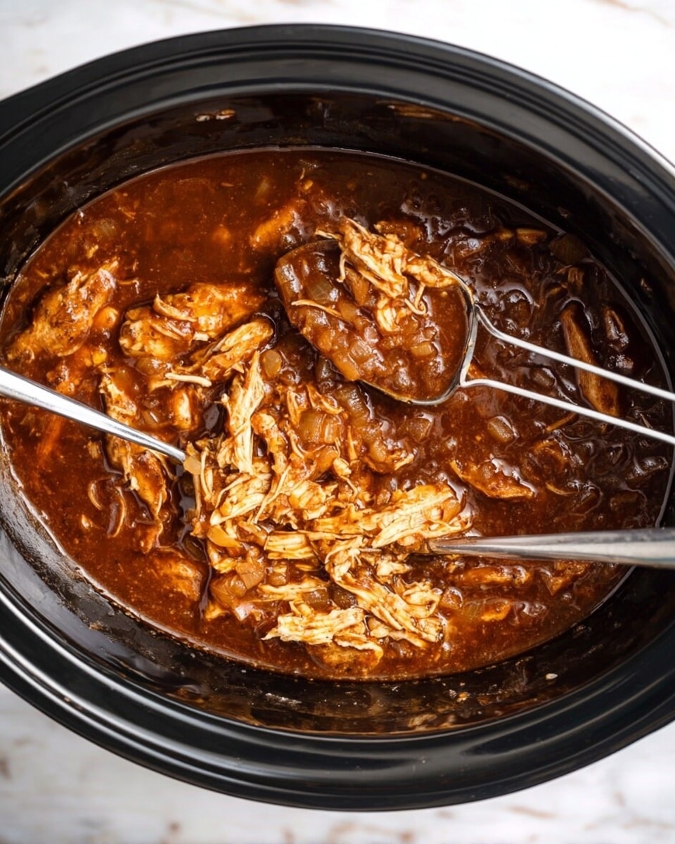 The image shows a black slow cooker filled with dark brown sauce covering several pieces of cooked chicken. The sauce has a thick texture with visible chopped onions mixed inside. Two silver forks are placed inside the cooker, one lifting and pulling apart a piece of the light brown shredded chicken. The slow cooker is set on a white marbled surface. photo taken with an iphone --ar 4:5 --v 7