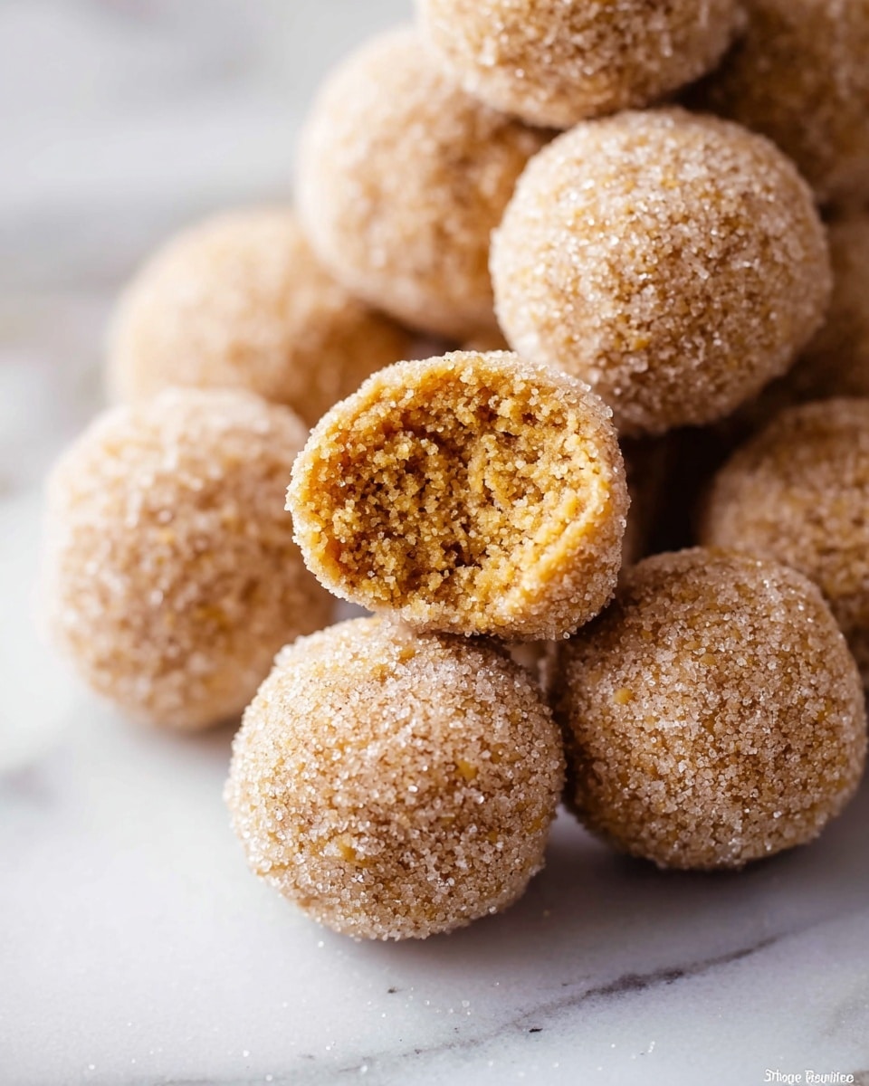 A close-up of small round balls covered in a light brown sugar coating, stacked loosely on a white marbled surface. The balls have a rough texture on the outside due to the sugar coating. One of the balls is broken open, revealing a soft, crumbly inside that is a warm golden brown color with a porous texture. The lighting highlights the granular sugar crystals and the soft interior clearly, creating a cozy, sweet appearance. Photo taken with an iphone --ar 4:5 --v 7