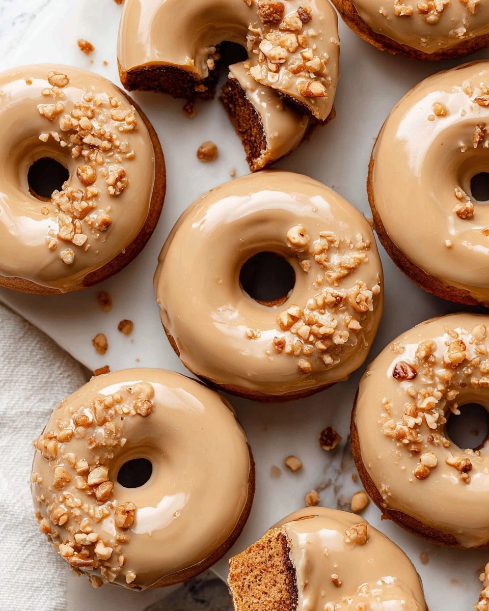 The image shows several tan-colored donuts with smooth, light brown icing topped with small crumbles placed on a white rectangular tray over a white marbled surface. The donuts are stacked and spread out, with two of them partially eaten, revealing a soft, fluffy, brown inside. There is a small white bowl filled with the same crumble on the lower left side on top of a patterned white cloth. Two cups filled with coffee sit near the top, one with a woman's hand holding it, along with a coffee carafe filled with dark coffee. The whole scene is bright and cozy with a clean, white marbled background. photo taken with an iphone --ar 4:5 --v 7