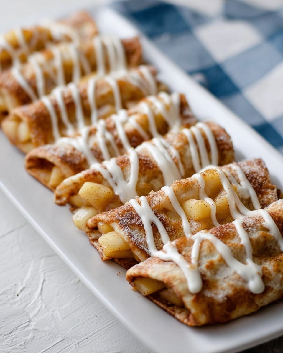 A long white plate holds a row of small folded flatbreads, each layered with a golden mixture of diced cooked apples and cinnamon that is soft and slightly shiny. The flatbreads have a warm, light brown color with a textured, slightly crisp look at the edges. On top, white creamy drizzle is evenly painted in thin lines along the length of the flatbreads. The background features a white marbled texture with soft light and a hint of a blue and white checkered cloth on the side. photo taken with an iphone --ar 4:5 --v 7