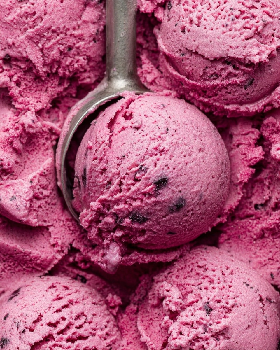 A close-up view of several scoops of deep pink ice cream with small darker specks mixed throughout. The texture looks creamy but a bit rough with some uneven patches and soft edges. A metal ice cream scoop is partially shown, holding one scoop near the center of the image. The ice cream fills the whole frame with no visible container, and the background is a white marbled texture. photo taken with an iphone --ar 4:5 --v 7
