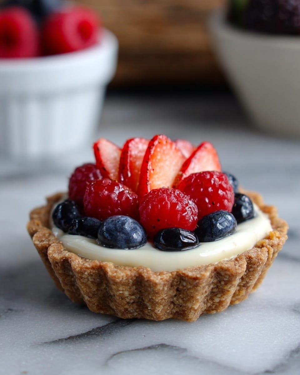 A small tart with a light brown, crumbly crust at the bottom, filled with a smooth white cream. On top, there are sliced red strawberries arranged in a fan shape in the center, surrounded by shiny red raspberries and dark blue blueberries all placed closely together. The tart sits on a white marbled surface with a blurred white bowl of berries in the background. Photo taken with an iphone --ar 4:5 --v 7