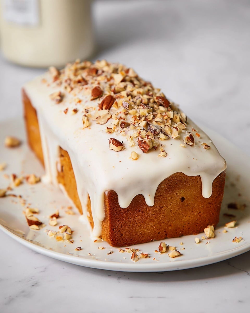 A rectangular cake sits on a plain white plate with a white marbled background. The cake has one visible layer of golden-brown sponge. It is topped with a thick white icing that drips slightly down the sides. On top of the icing, there is a generous sprinkling of chopped nuts, varying shades of brown, adding texture and color contrast. Small pieces of nuts scatter around the plate, enhancing the rustic look. photo taken with an iphone --ar 4:5 --v 7