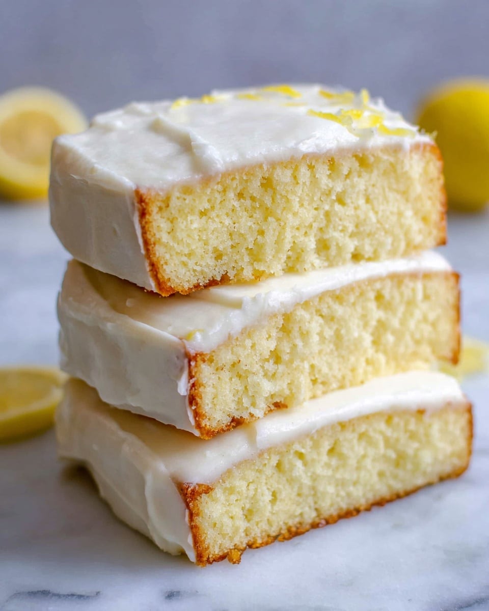 The image shows a stack of three thick slices of light yellow cake, each layer covered with a smooth white frosting on the sides. The cake layers are soft and slightly crumbly with a moist texture. The white frosting has a creamy look with some gentle folds and slight unevenness. The stack sits on a white marbled surface with parts of lemons visible at the corners, adding a bright yellow contrast to the warm, pale tones of the cake. photo taken with an iphone --ar 4:5 --v 7