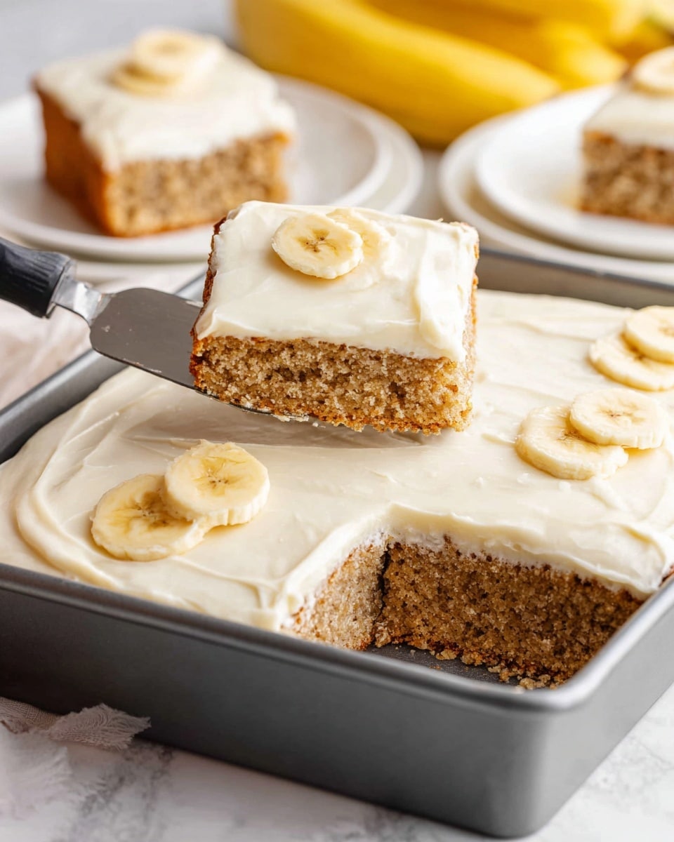 The image shows a rectangular banana cake in a gray baking pan placed on a white marbled surface. The cake has two visible layers: a bottom layer with a light brown, soft, and crumbly texture, and a top thick layer of smooth, creamy white frosting spread evenly across the surface. Three slices of banana are placed on top of the frosting, one on each of the three cut squares. A spatula lifts one square piece of cake from the pan, and in the background, there are two pieces of cake on white plates, along with a bunch of yellow bananas. Photo taken with an iphone --ar 4:5 --v 7
