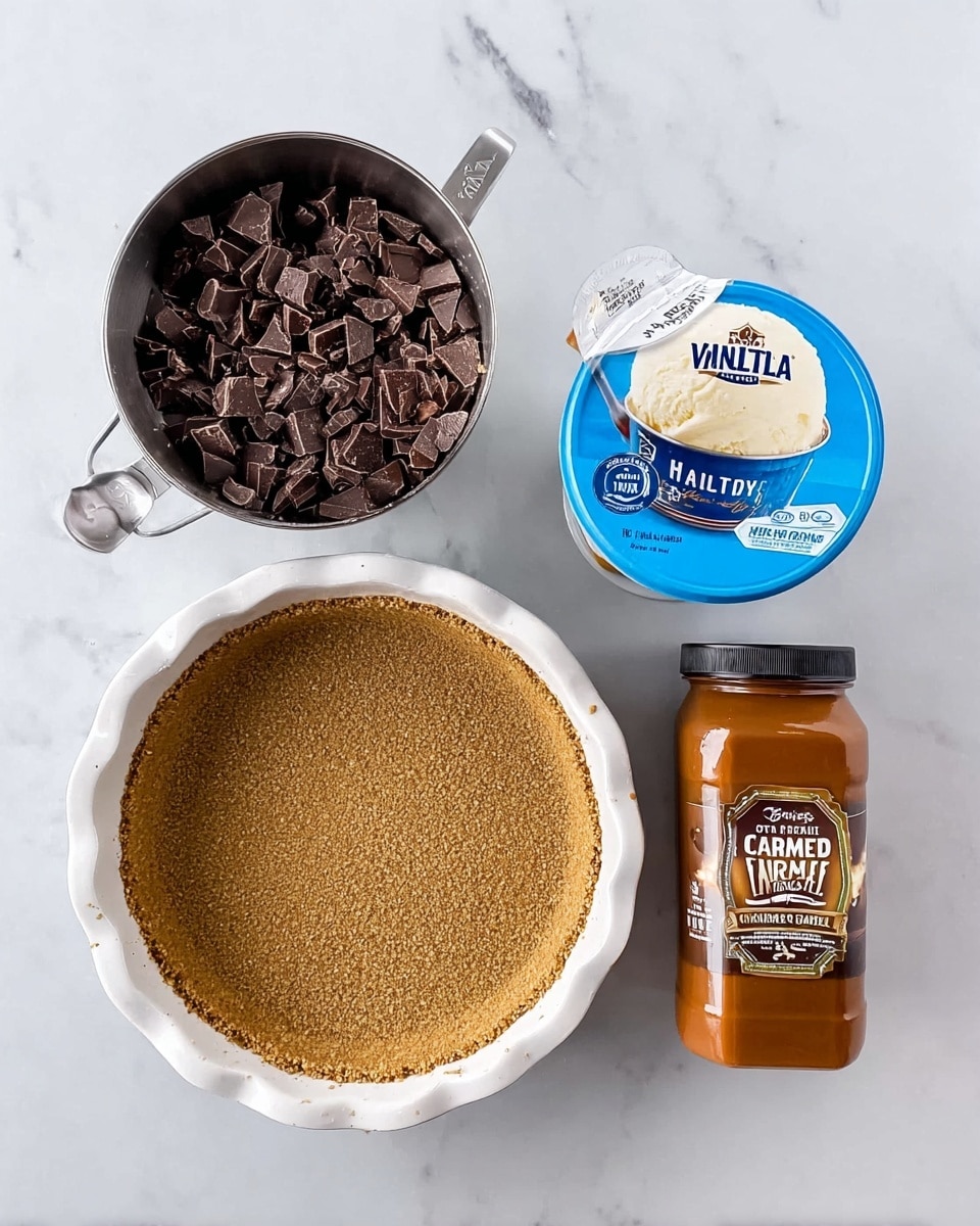 A white pie pan with a graham cracker crust is on the left side on a white marbled surface. Next to the pie pan is a half cup measuring cup filled with chopped dark chocolate pieces. To the right of that is a blue and cream ice cream container labeled