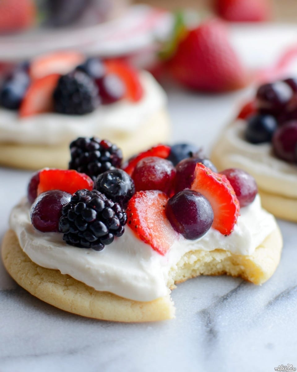 The image shows a two-layer round cookie that is light golden in color, with a bite taken out of the front. On top of the cookie is a thick layer of white creamy frosting, smooth in texture. The frosting is topped with fresh fruits: sliced red strawberries, dark purple blueberries, blackberries, and red grapes, arranged closely together. In the background, there is a blurred view of another similar cookie with the same topping, all set on a white marbled surface. The image is close-up and sharp on the nearest cookie, with soft lighting highlighting the freshness of the fruit. Photo taken with an iphone --ar 4:5 --v 7