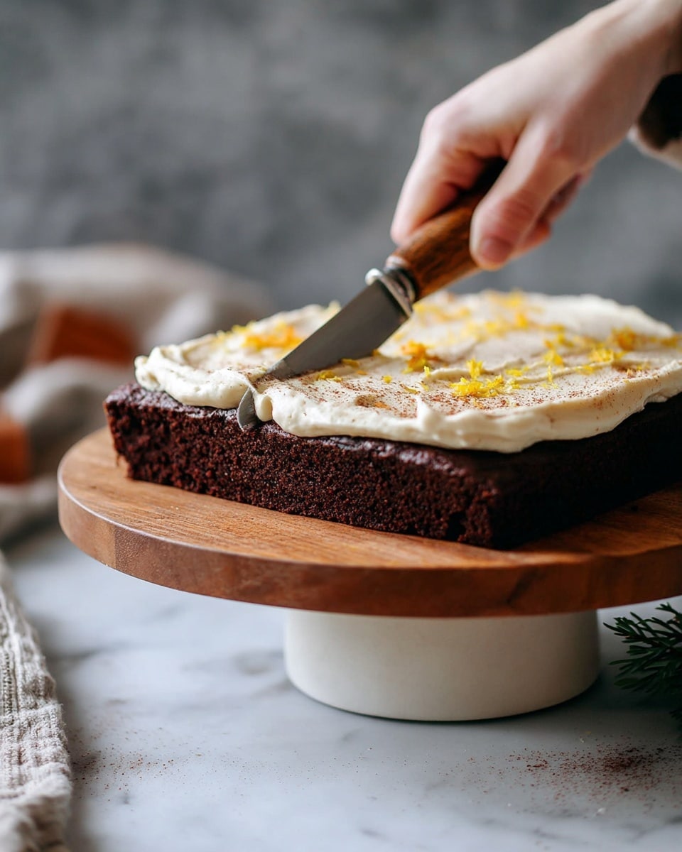 A close-up view of a square dark brown chocolate cake with a thick creamy white frosting spread evenly on top. The frosting has a slightly rough texture and is sprinkled with small yellow bits and a light dusting of brown powder. The cake is placed on a round wooden cake stand with a white base, held by a woman's hand using a small knife with a wooden handle and silver blade, slightly lifting the edge of the frosting. The background features a soft white marbled surface beneath the stand and an out-of-focus faint gray and brown area behind. Photo taken with an iphone --ar 4:5 --v 7