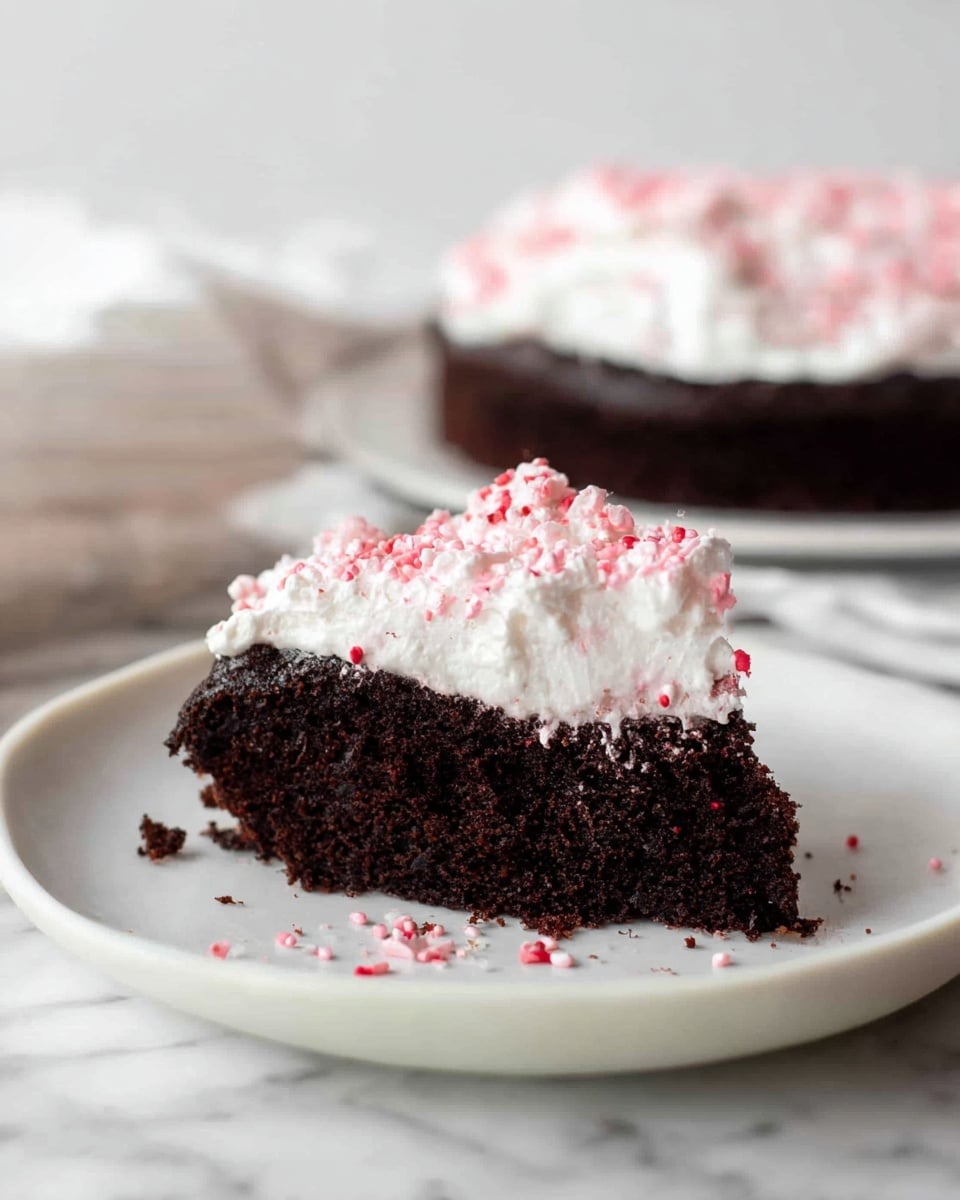 A round chocolate cake sits on a white marbled surface, with a thick, dark brown base layer that looks moist and dense. On top of the cake is a thick layer of fluffy white whipped cream spread unevenly, creating soft peaks and swirls. The whipped cream is sprinkled with small red and white peppermint pieces, adding a touch of color and texture. Above the cake, a woman's hand is gently sprinkling more crushed peppermint pieces. Photo taken with an iphone --ar 4:5 --v 7