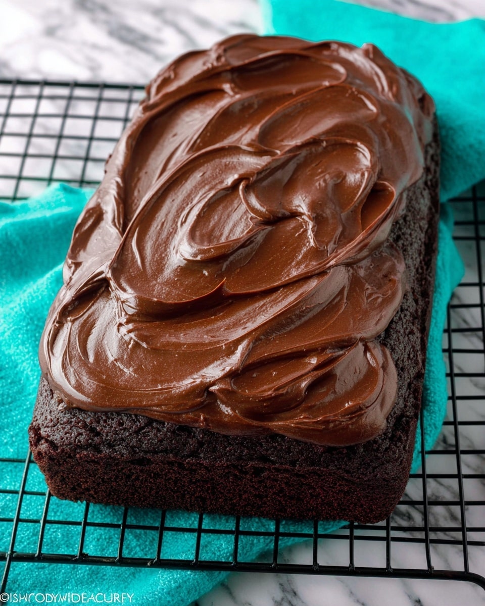 A single rectangular chocolate cake with a dark, rich brown base layer topped with a thick, glossy, smooth layer of chocolate frosting spread unevenly with visible swirls and waves across the top. The cake sits on a black cooling rack with a bright teal cloth partially visible underneath, all on a white marbled surface. photo taken with an iphone --ar 4:5 --v 7