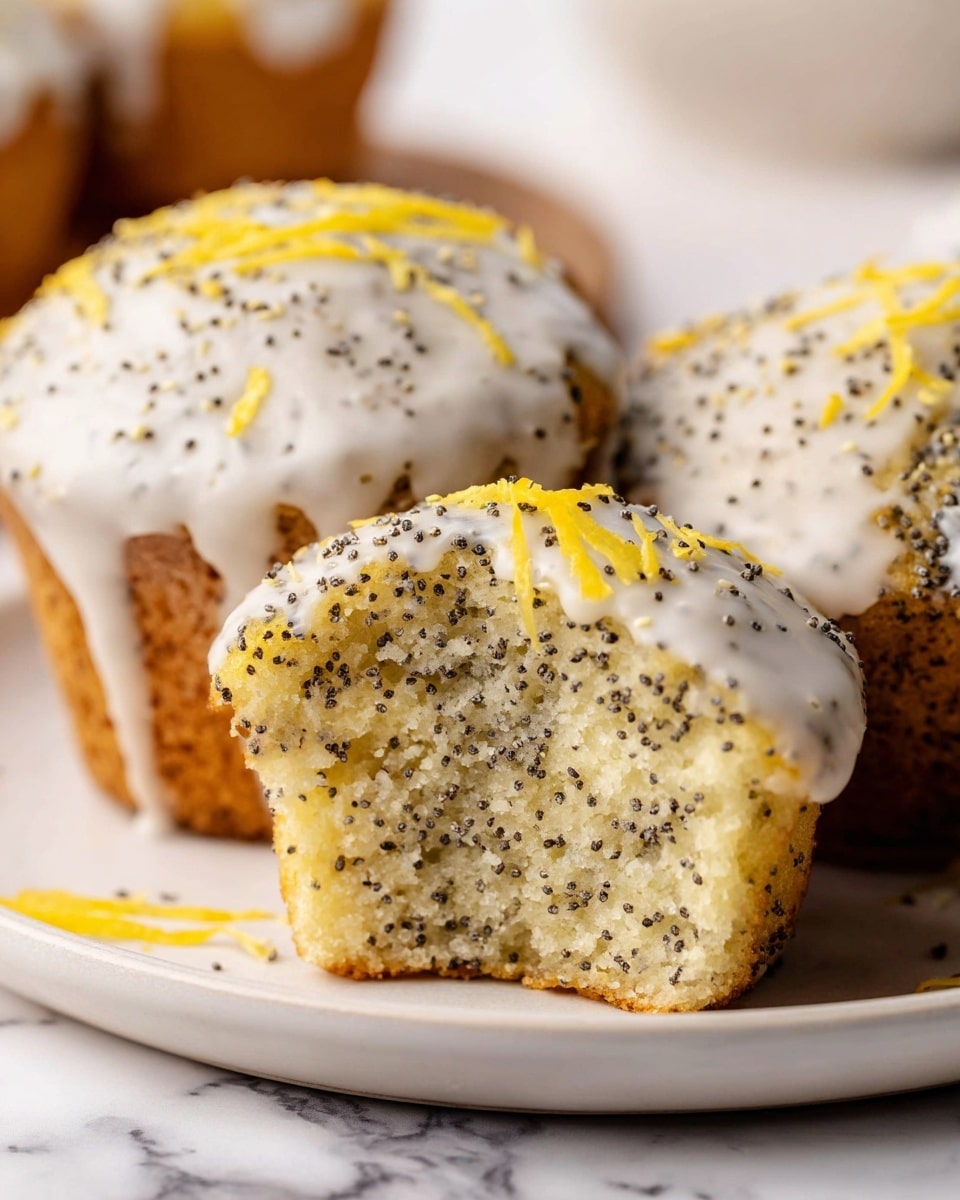 The image shows three lemon poppy seed muffins on a white plate over a white marbled surface. Two whole muffins sit side by side, covered with a smooth white icing that drips slightly over their sides, each topped with small black poppy seeds and thin strips of bright yellow lemon zest. One muffin is positioned in front, cut in half to reveal a soft, light-colored crumb inside that is full of small black poppy seeds, giving the texture a speckled look. The overall colors are pale yellow and white, with poppy seeds adding tiny black dots throughout. Photo taken with an iphone --ar 4:5 --v 7