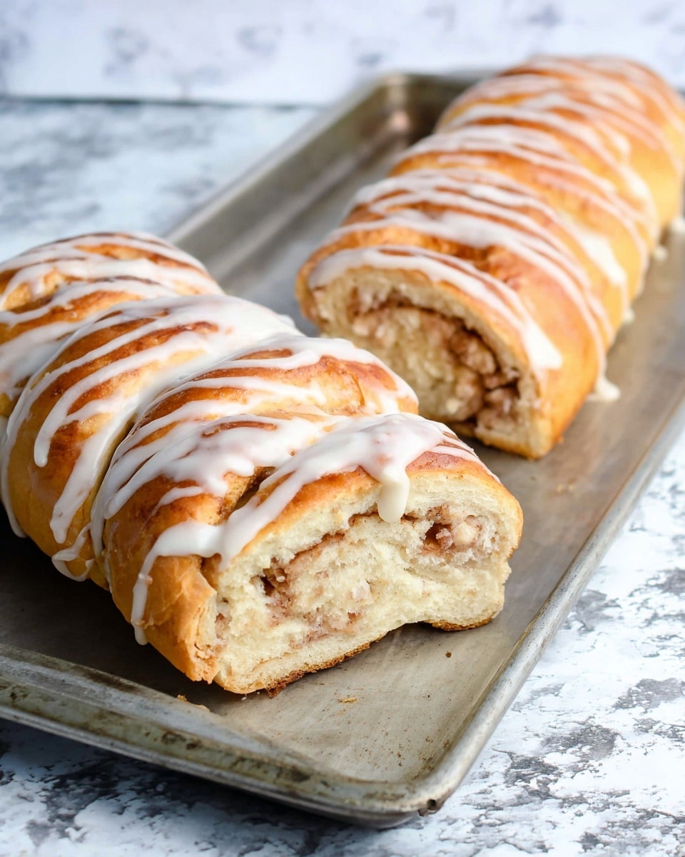 A long cinnamon roll with a golden brown outside covered with white icing drizzle sits on a metal baking tray. One roll is whole, showing shiny, smooth, and slightly cracked texture, while the other is partially sliced, revealing a soft inside with swirls of cinnamon sugar filling that are light brown mixed with the cream dough. The background is a white marbled texture. photo taken with an iphone --ar 4:5 --v 7
