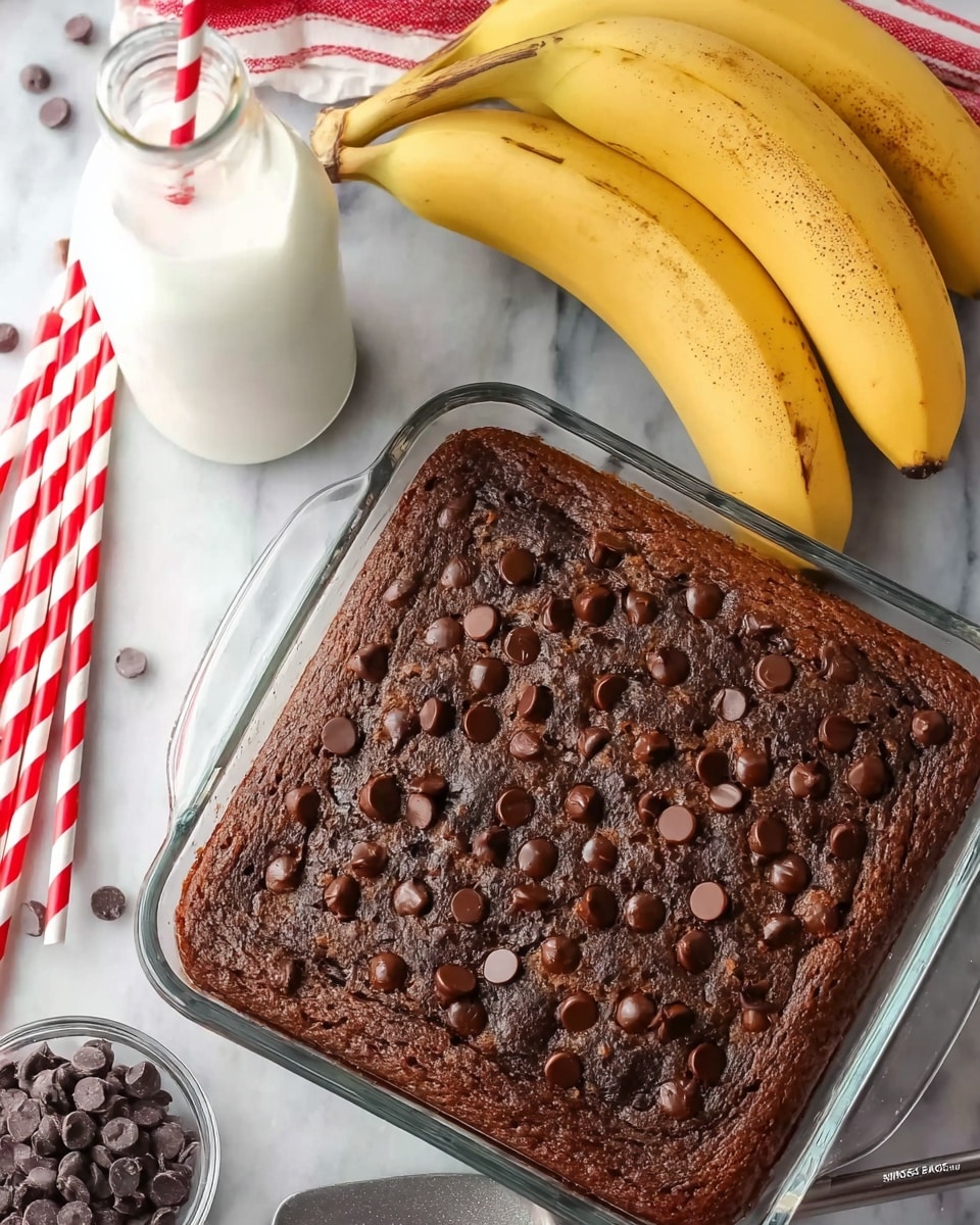 A close-up view of a freshly baked chocolate chip banana cake in a clear glass square baking dish, with a dark brown top layer studded evenly with small, shiny chocolate chips creating a textured surface. The dish is placed on a white marbled surface, nearby a bunch of three ripe yellow bananas with brown speckles on their peel and a small pile of dark chocolate chips. In the background, there is a glass bottle filled with milk with a red and white striped straw inside it, and several more red and white striped straws lying around. A metal spatula with a black handle rests beside the baking dish. The overall scene has a bright and homemade vibe. photo taken with an iphone --ar 4:5 --v 7
