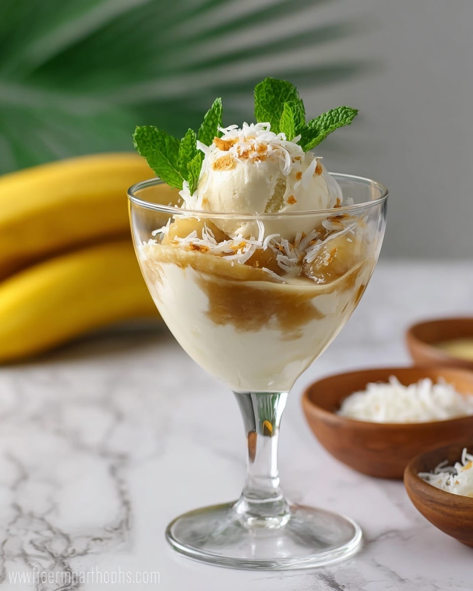 This dessert is served in a clear glass with a stem, showing three layers inside. The bottom layer is smooth and white, like yogurt or cream. The middle layer is a thick, light brown sauce with soft fruit pieces mixed in. The top layer is a scoop of white ice cream or cream, sprinkled with shredded white coconut and small crunchy bits. On top, there are three fresh green mint leaves adding color. In the background, there are two yellow bananas and small bowls with more shredded coconut on a white marbled surface. Photo taken with an iphone --ar 4:5 --v 7