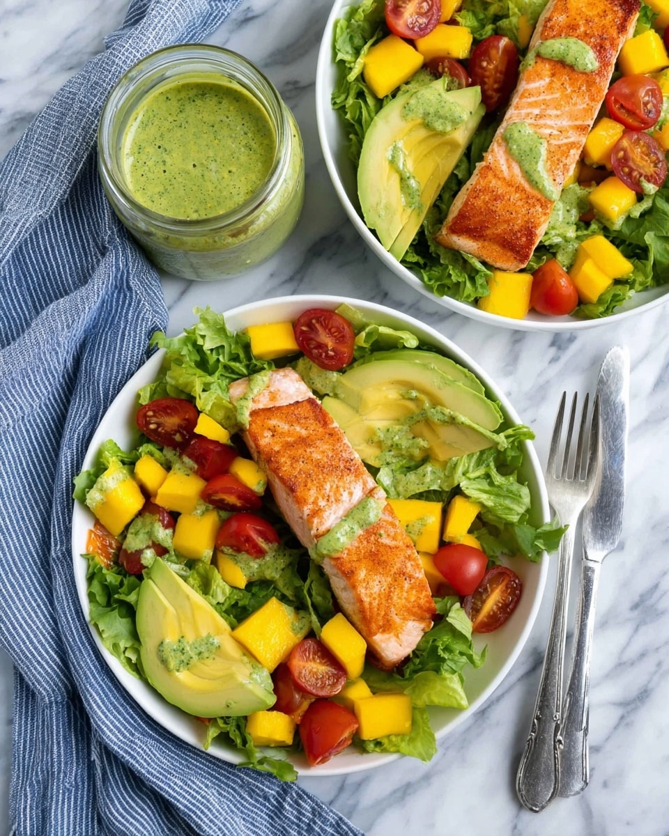 Two white bowls are filled with fresh green lettuce as the base layer, topped with bright red cherry tomato halves and yellow mango cubes scattered throughout. On one edge of the bowls, there are smooth, green slices of avocado, while a golden-brown cooked salmon fillet rests diagonally on top. Small dollops of green herb sauce are drizzled over the salmon and avocado, adding texture and color. The bowls sit on a white marbled surface, next to a glass jar filled with the same green sauce and a spoon inside. Two forks rest nearby on a blue and white striped cloth. Photo taken with an iphone --ar 4:5 --v 7