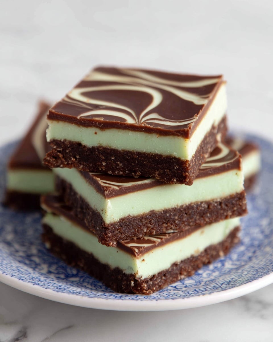 The image shows two squares of layered dessert stacked on top of each other against a white marbled background. Each square has three layers: the bottom layer is a thick, crumbly dark brown base with a rough texture; the middle layer is a smooth, light green cream; the top layer is a shiny, solid dark brown chocolate. Small crumbs are visible around the dessert on the surface. photo taken with an iphone --ar 4:5 --v 7