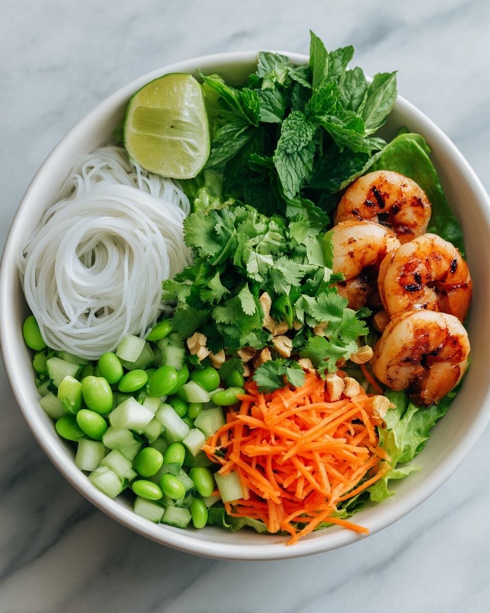 A white bowl holds a colorful layered dish on a white marbled surface. The bottom layer is fresh, dark green leafy lettuce mixed with bright green edamame beans. On top of that, there are chopped light green cucumber pieces and diced pale green avocado pieces placed side by side. Next to them, there is a small pile of thin, white rice noodles that look soft and smooth. At the center, shredded bright orange carrots sprinkled with chopped nuts and fresh cilantro leaves are layered. Two grilled shrimp with a slightly charred orange and pink shell are placed on the edge of the bowl, along with a wedge of lime. The scene includes a small white bowl with a reddish-brown sauce in the background. Photo taken with an iphone --ar 4:5 --v 7