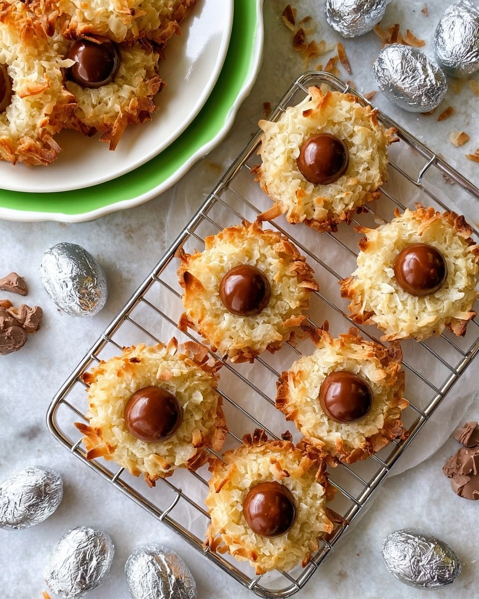 The image shows a white rectangular tray with a metal cooling rack holding seven coconut cookies topped with a single chocolate drop in the center of each cookie. Each cookie has a rough, golden-brown toasted texture with shredded coconut forming a ring around the glossy, smooth chocolate drop in the middle. Scattered around the tray and on the white marbled surface are more loose chocolate drops and silver wrapped candies. In the top left, a white plate with a green rim holds additional cookies. The overall look is bright with warm tones from the toasted coconut and rich brown from the chocolate drops. Photo taken with an iphone --ar 4:5 --v 7