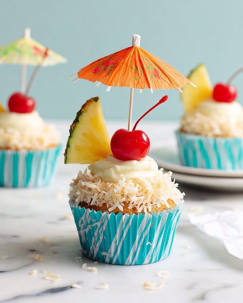 A single cupcake in a turquoise and white striped wrapper stands centered on a white marbled surface. The cupcake has one light brown base layer topped with a thick layer of white frosting covered in shredded coconut giving a rough texture around the sides. On top, a bright red cherry with a long stem and a small triangular slice of pineapple with yellow flesh and green rind are placed. A small orange cocktail umbrella stands open at the back of the cupcake, adding a tropical look. In the background, two more similarly decorated cupcakes and a white plate are slightly blurred. Photo taken with an iphone --ar 4:5 --v 7