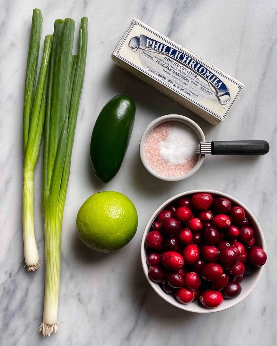 The image shows several ingredients arranged on a white marbled surface: two long green onions on the left, a bright green lime next to a dark green jalapeño pepper in the middle, a silver box of Philadelphia original cream cheese below the lime and jalapeño, a small white bowl filled with white granulated sugar above the cream cheese, and a black-handled measuring spoon filled with pink salt resting on the edge of the sugar bowl. On the right side, there is a white bowl filled with fresh red cranberries. Photo taken with an iphone --ar 4:5 --v 7