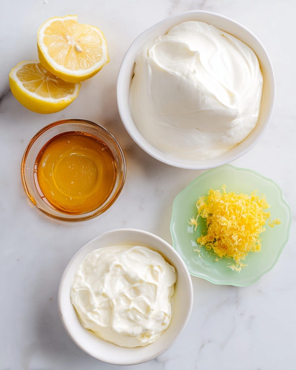 Top view of four white bowls on a white marbled surface, each with different ingredients. The largest bowl at top right is filled with a thick layer of smooth, white cream. Below it is a smaller white bowl filled with a lighter, fluffier white cream. To the left is a clear bowl containing a thick, shiny golden yellow honey layer. Next to it at the top left is a small white bowl with textured yellow lemon zest. Two halves of a lemon sit on the surface, one on a pale green glass plate and the other directly on the marbled background. photo taken with an iphone --ar 4:5 --v 7