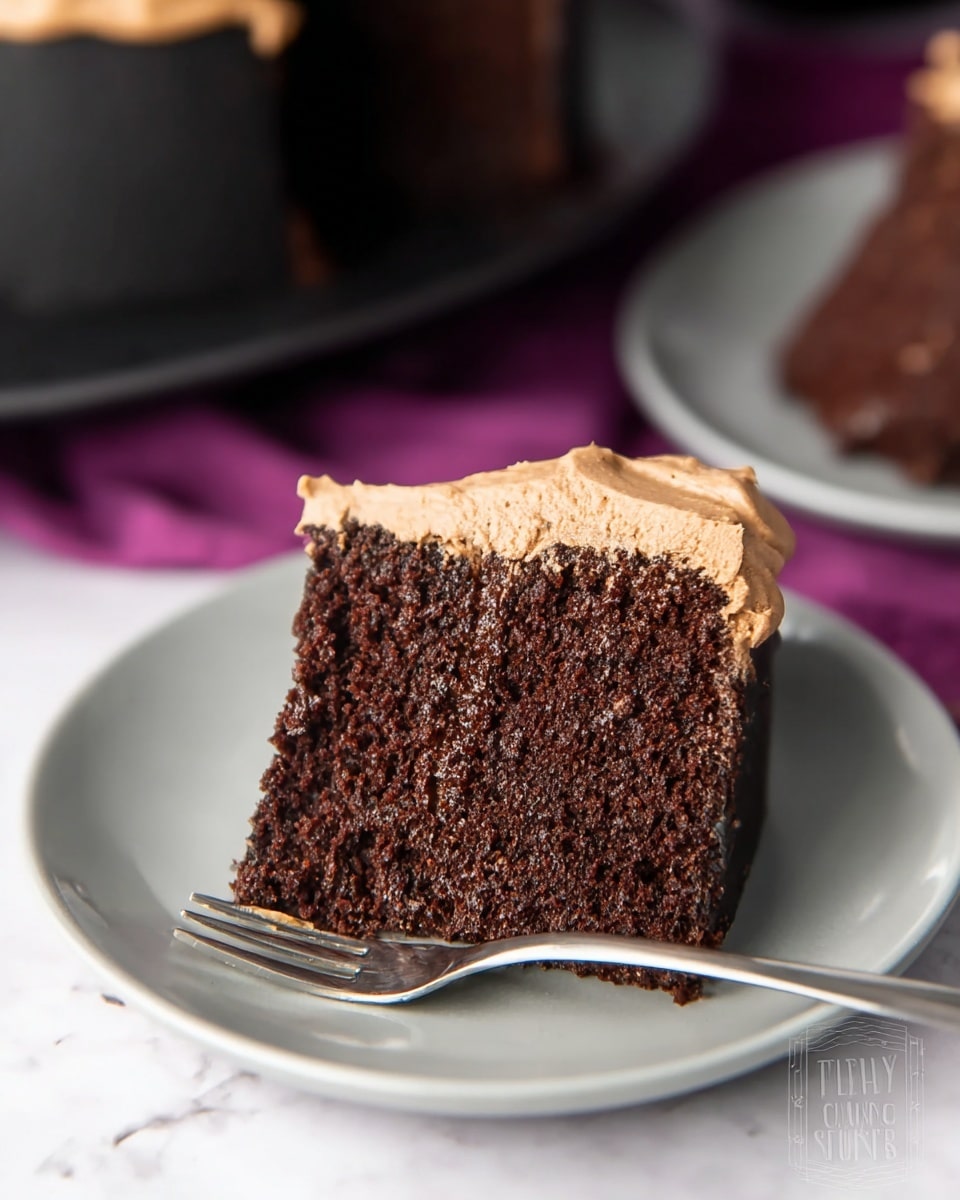 A slice of chocolate cake with one thick layer of dark brown moist cake and a light brown creamy frosting layer on top. The slice sits on a white plate with a simple fork placed next to it. The background is a white marbled texture with some blurred elements behind the plate, focusing on the cake slice in the center. The cake texture looks soft and rich with the frosting smooth and creamy. Photo taken with an iphone --ar 4:5 --v 7