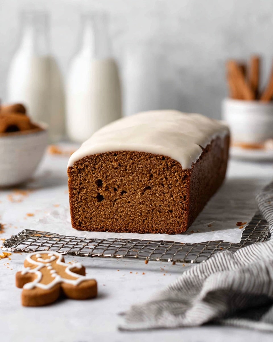A loaf of brown gingerbread cake with a smooth, creamy white icing layer on top, placed on a white parchment paper over a silver cooling rack. The cake shows a dense, moist texture inside with small air bubbles. In front of the rack, there are two small gingerbread cookies on a white marbled surface. In the blurred background, there are two white bottles, a white bowl with cinnamon sticks, and a gray striped cloth on the right side. Photo taken with an iphone --ar 4:5 --v 7