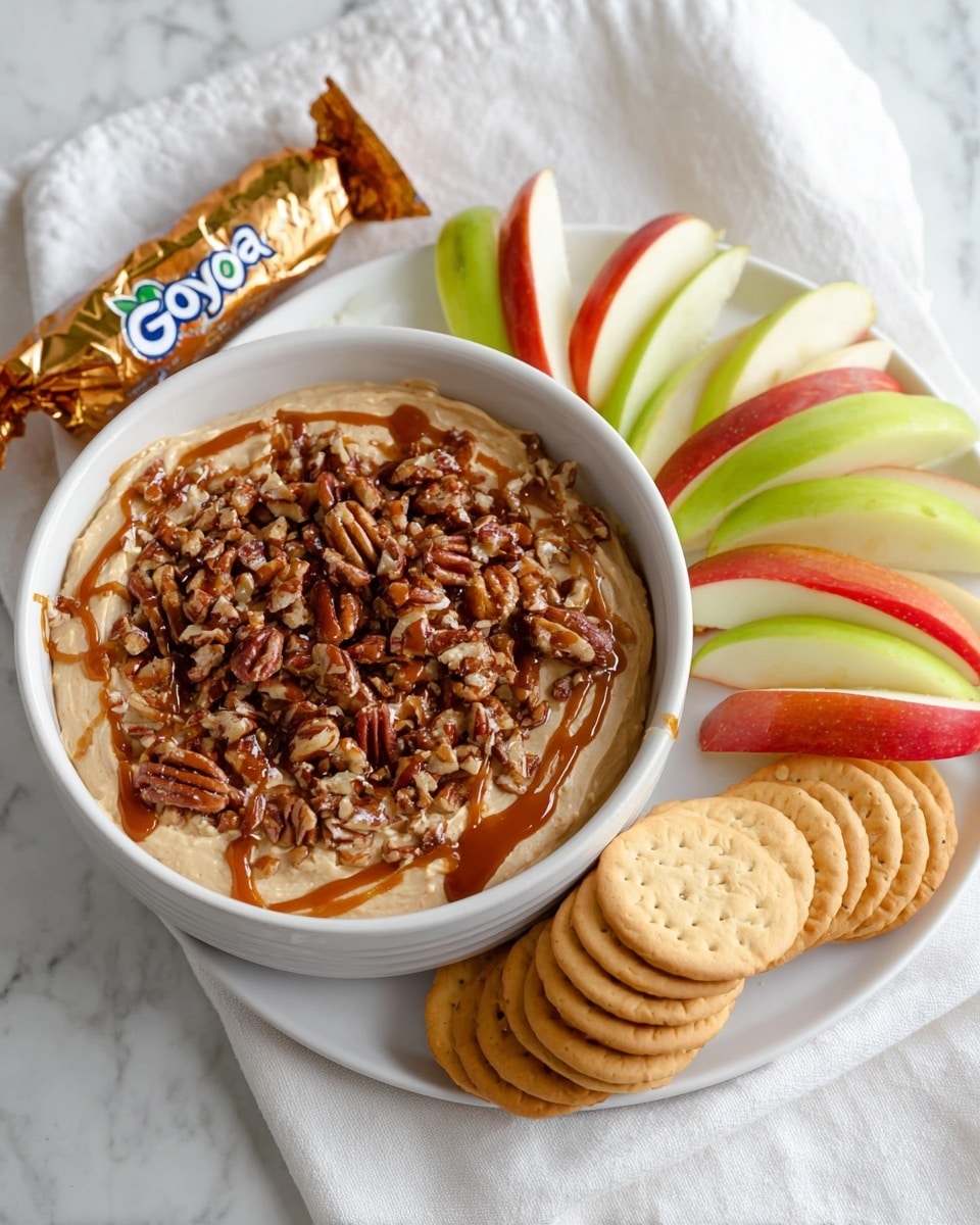 The image shows a white bowl filled with a dip that has three visible layers: a smooth beige base, a thick layer of chopped pecans covering the surface, and a drizzle of light brown caramel sauce on top. The bowl is set on a white plate with neatly arranged slices of red and green apples fanned out along one side and a small stack of beige round cookies lying flat on the other side. A shiny gold wrapper of Goya Maria Cookies is placed next to the plate on a white marbled surface, with a white cloth partially underneath. Photo taken with an iphone --ar 4:5 --v 7