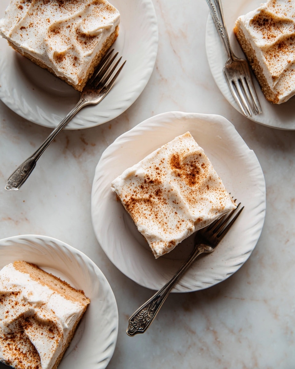 Three white plates rest on a white marbled surface, each holding a square piece of cake with two layers. The bottom layer is a light brown cake, soft and moist, while the top layer is a smooth, creamy white frosting sprinkled with a fine dusting of brown spice. Each cake piece has a vintage silver fork beside it, and the frosting shows gentle, uneven swirls giving a textured look. The light softly highlights the creamy frosting and the matte texture of the cake. Photo taken with an iphone --ar 4:5 --v 7