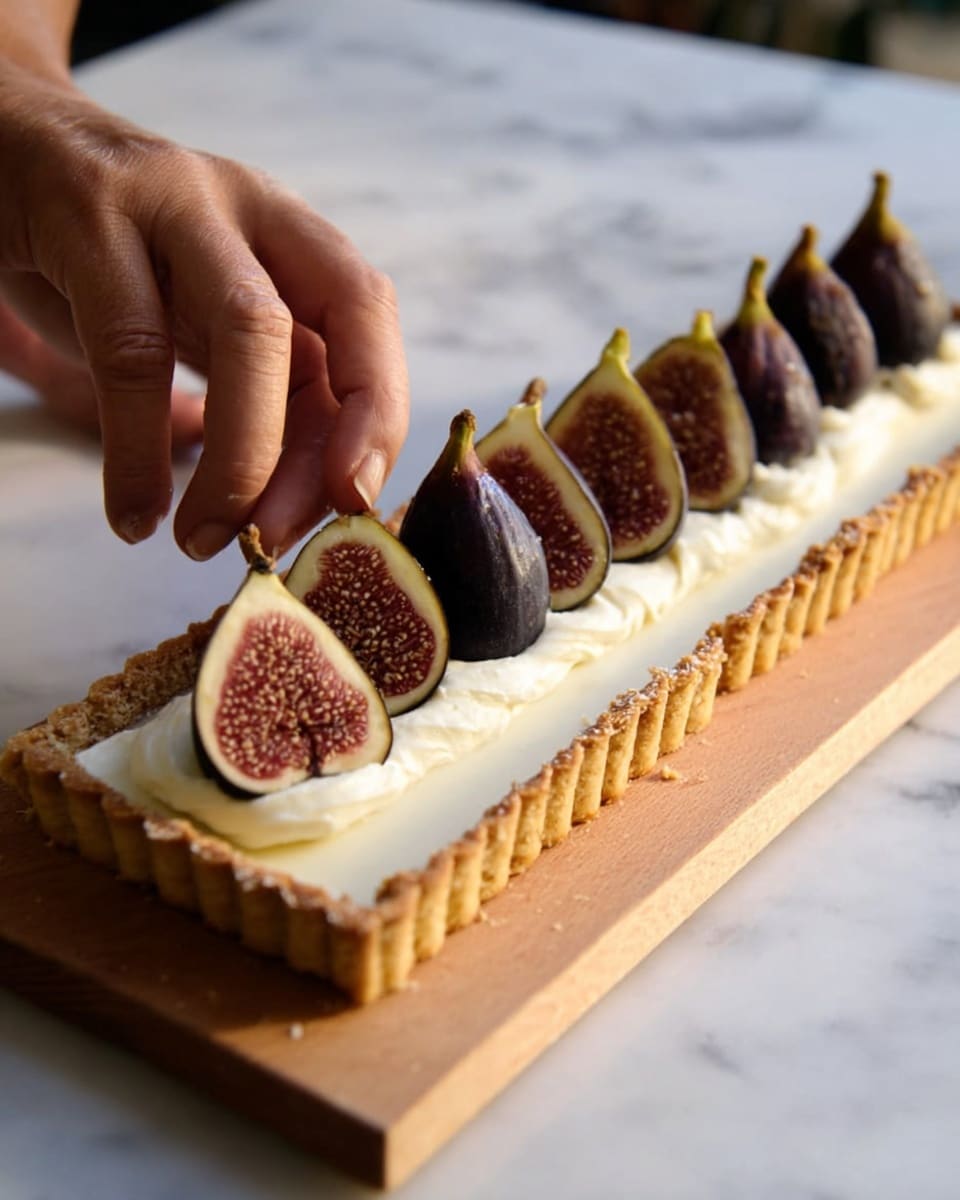 A rectangular tart with a golden-brown crust forms the base, filled with a thick, smooth white cream layer that almost reaches the crust's edges. On top, a row of eight whole dark purple figs is carefully placed in two parallel lines along the length of the tart. A woman's hand is gently positioning one of the figs near the front center. The tart rests on a wooden board, which sits on a white marbled surface, with soft natural lighting that highlights the textures of the crust, cream, and figs. photo taken with an iphone --ar 4:5 --v 7